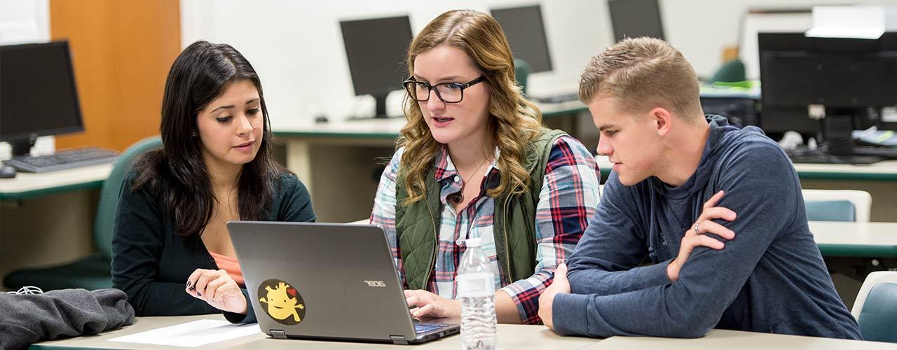 Three students discuss around a laptop