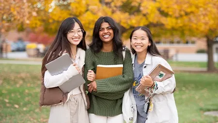 Three friends smiling and holding schoolbooks.