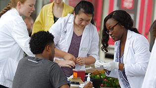 Students in white lab coats standing around a table preparing pharmacy supplies.